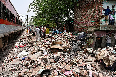 People gather near debris during an anti-encroachment drive carried out by administrative officials along the railway line near Daya Basti Railway Station, in New Delhi.