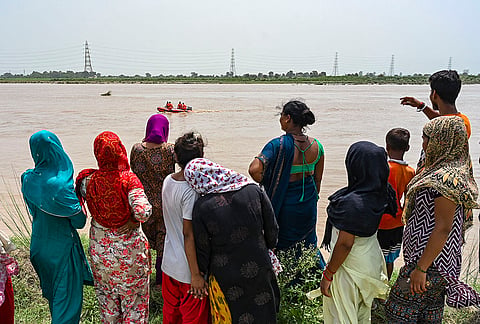 People gather as rescue personnel carry out an operation after four minors allegedly drowned after they were swept away by the Yamuna river's strong current while bathing on Sunday, near Hiranki village in New Delhi.