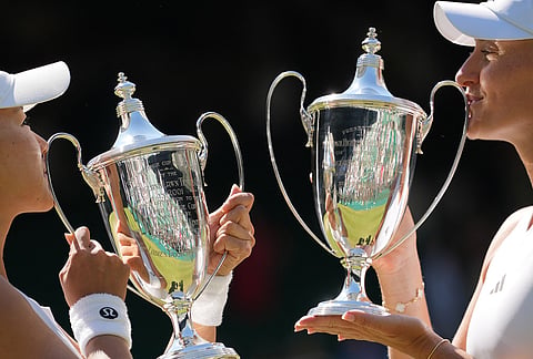 Kristina Mladenovic of France, right, and playing partner Hanyo Guo of China kiss the winners trophies after defeating Luisa Stefani of Brazil and Gabriela Dabrowski of Canada, in the women's doubles final at Wimbledon Tennis Championships in London.
