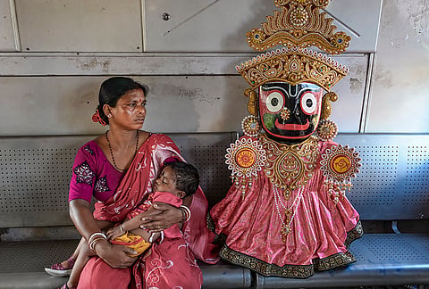 A woman carrying a child sits beside an idol of Lord Jagannath being transported to Kolkata for the Rath Yatra, in Nadia, West Bengal.