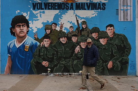 A man walks past a street mural depicting late soccer star Diego Maradona and veterans of the 1982 war 