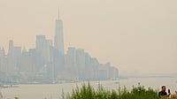 (AP Photo/Seth Wenig) : The New York City skyline, shrouded in smoke, is used as a backdrop for a man recording himself in Weehawken, N.J., Thursday, July 16, 2026