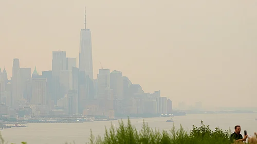 (AP Photo/Seth Wenig) : The New York City skyline, shrouded in smoke, is used as a backdrop for a man recording himself in Weehawken, N.J., Thursday, July 16, 2026
