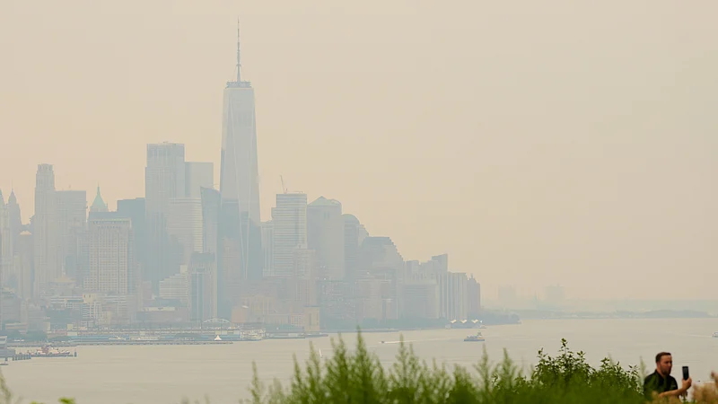 (AP Photo/Seth Wenig) : The New York City skyline, shrouded in smoke, is used as a backdrop for a man recording himself in Weehawken, N.J., Thursday, July 16, 2026