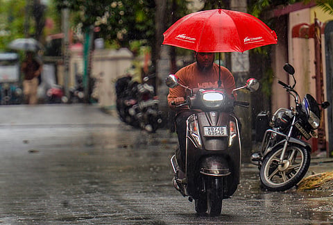 A commuter covers himself amid rainfall, in Siliguri, West Bengal.