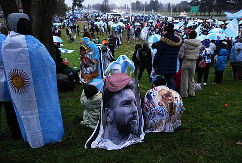 An Argentina fan wrapped in a flag bearing an image of Lionel Messi gathers outside the Argentine Football Association headquarters while waiting for the national team to arrive in Ezeiza, on the outskirts of Buenos Aires, Monday, July 20, 2026, following its World Cup final loss to Spain. 