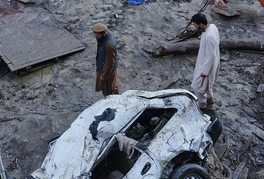 Residents walk past a vehicle damaged by heavy flooding in the eastern province of Nuristan, Afghanistan, Tuesday, July 21, 2026. 