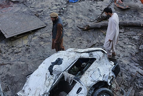 Residents walk past a vehicle damaged by heavy flooding in the eastern province of Nuristan, Afghanistan, Tuesday, July 21, 2026. 