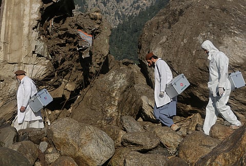 Medical workers carry equipment through an area damaged by heavy flooding in the eastern province of Nuristan, Afghanistan, Tuesday, July 21, 2026. 