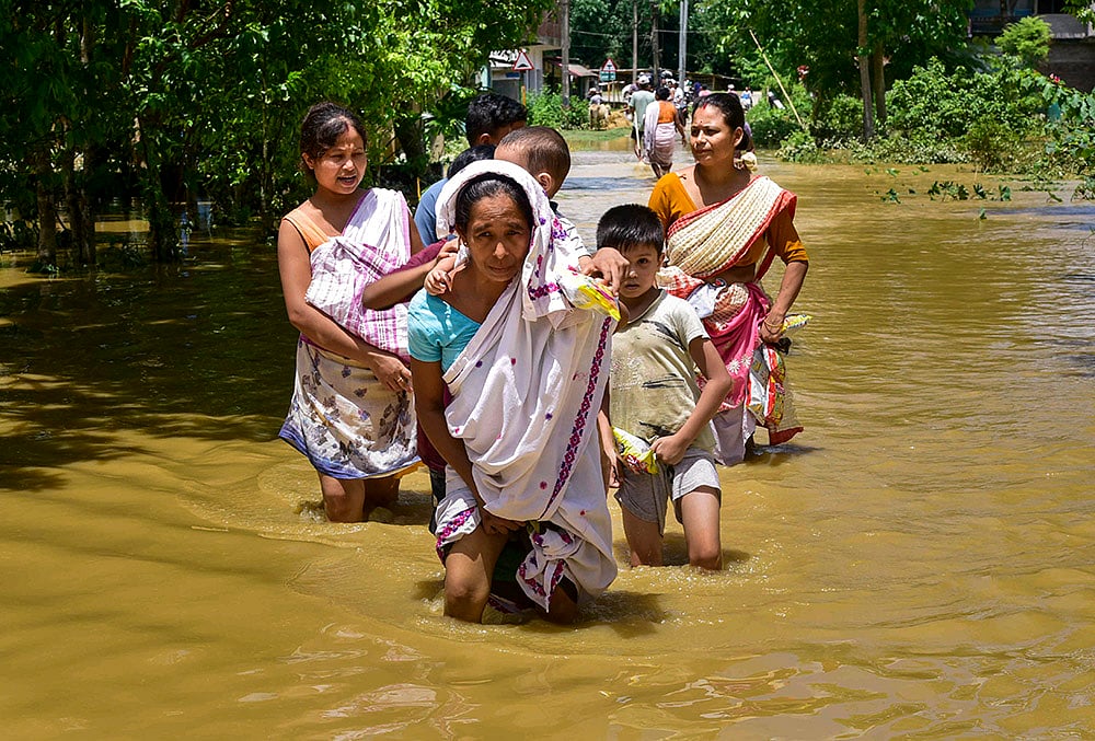 People move to a safer place in a flood-affected area following incessant heavy rainfall, at Phulpanisiga in Sivasagar district, Assam, Tuesday, July 21, 2026.  - | Photo: PTI