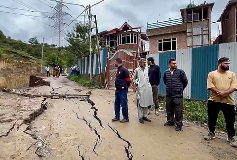 People stand near a road damaged by a landslide following heavy rainfall, in Baramulla district, Jammu and Kashmir, Wednesday, July 22, 2026. 