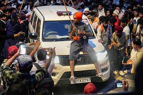A volunteer sits on the bonnet of a Delhi Police vehicle and helps clear the way through a crowd of protesters during the ongoing demonstration over the NEET-UG issue, at Parliament Street, in New Delhi.