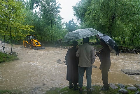 People look at the earthmoving machines clearing an overflowing stream following floods and rainfall, in Khag area, Budgam district, Jammu and Kashmir, Wednesday, July 22, 2026. 