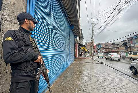 A security official stands guard amid intensified search operations across several areas to track down the assailant who shot dead a police official a day earlier, in Anantnag district, Jammu and Kashmir.