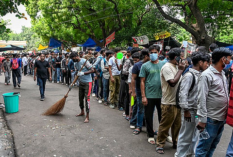 A sanitation worker sweeps the road as people gather at Jantar Mantar during the ongoing protest demanding the resignation of Union Education Minister Dharmendra Pradhan over the NEET paper leak issue, in New Delhi.