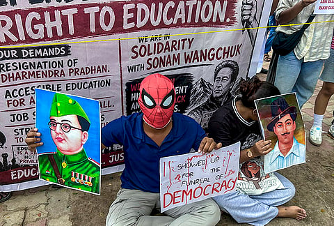 A demonstrator wearing a Spiderman mask holds a portrait of Netaji Subhash Chandra Bose and a placard during the ongoing protest demanding the resignation of Union Education Minister Dharmendra Pradhan over the NEET paper leak issue, in Agartala, Tripura. 