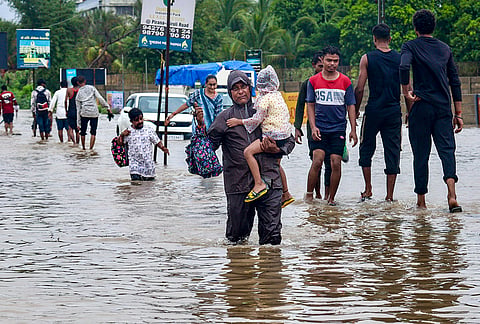 People wade through a waterlogged road following heavy rainfall, in the outskirts of Ahmedabad, Gujarat, Friday, July 24, 2026. 