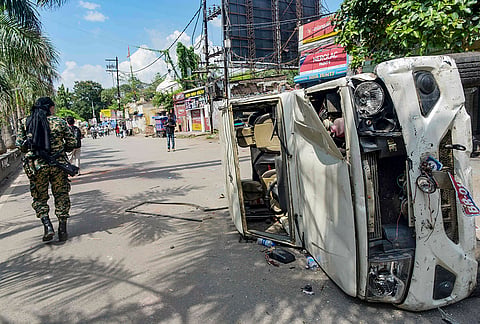 A security official near a vandalized vehicle during the 'Bihar Bandh' called over the alleged NEET paper leak and police action against protesting students, in Patna, Bihar.