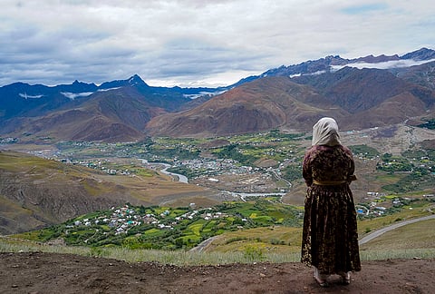 A woman looks at the view of Drass town with peaks including Batra Top, India Gate, Tiger Hill, PT 5165, and PT 5240 in the backdrop, in Drass district, Ladakh.