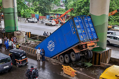People gather after a container truck driver was injured as the vehicle plunged into a 10-foot-deep pit dug for a water tank as part of Metro bridge work, in Thane, Maharashtra.