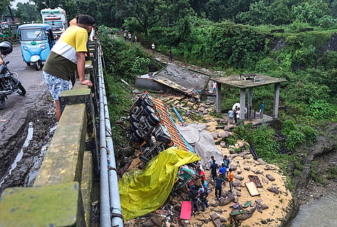 People gather near an overturned truck after it crashed through the safety railing of a bridge, in Kangra district, Himachal Pradesh.