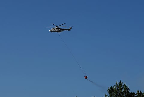 An Airbus helicopter lets a Bambi Bucket full of water go over a firezone near Lacanau, as wildfires rage outside Bordeaux, France, Monday, July 27, 2026. 