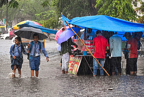 Students make their way through a waterlogged area as they return home from school amid heavy rain, in Noida. 