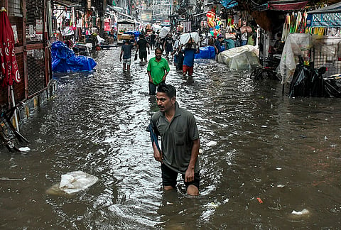 People wade through a waterlogged road amid heavy rainfall, in Sadar Bazaar area, in New Delhi.