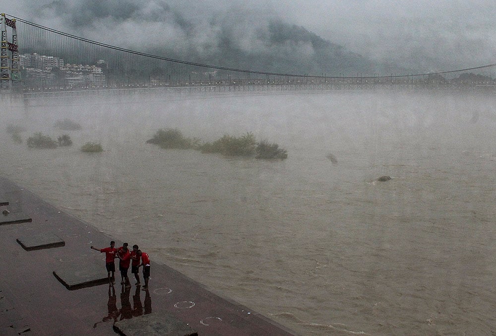 | Photo: PTI : People stand near the Janki Setu area amid rainfall, in Rishikesh, Uttarakhand.