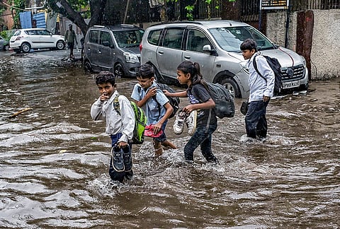 Children wade through a waterlogged road following heavy rainfall, in Jangpura-Bhogal area, in New Delhi, Tuesday, July 28, 2026. 