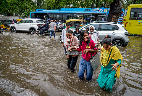 People wade through a waterlogged Jamia Millia Islamia road following heavy rain, in New Delhi, Tuesday, July 28, 2026. 