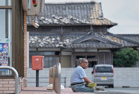 A person sits near a house damaged following an earthquake in Uki, Kumamoto Prefecture, southern Japan, Thursday, July 30, 2026.