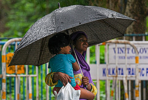 A woman carries a child as they cover themselves amid rainfall, in Kolkata, West Bengal.