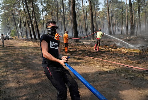 Local residents hose down smoldering fires in a forest in Souge, during wildfires in southwestern France, Wednesday, July 29, 2026. 