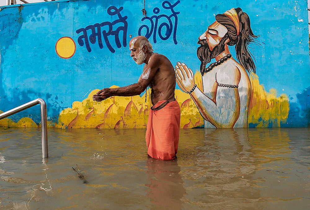 A sadhu offers prayers in the submerged section of Dashashwamedh Ghat after the water level of Ganga river rises, in Prayagraj, Uttar Pradesh. - | Photo: PTI