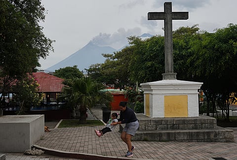 A woman playfully swings a child as clouds of ash rise from the crater of the Fuego volcano, as seen from San Pedro Las Huertas, Guatemala, Tuesday, Aug. 4, 2026. 