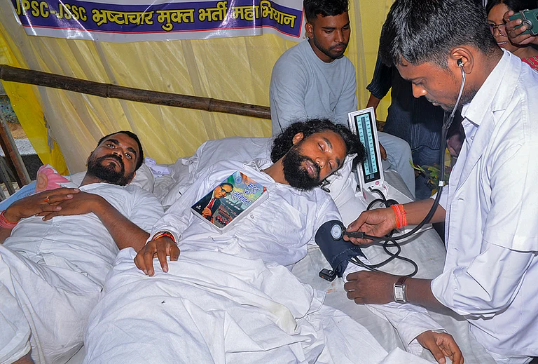 A medical worker checks the blood pressure of student leader Devendra Nath Mahto as he lies with a copy of the Constitution of India on his chest during an indefinite hunger strike at Jaipal Singh Munda Stadium, in Ranchi, Wednesday, Aug. 5, 2026. Mahto and fellow protesters are demanding a probe into alleged recruitment exam irregularities conducted by the JPSC and JSSC. - | Photo: PTI