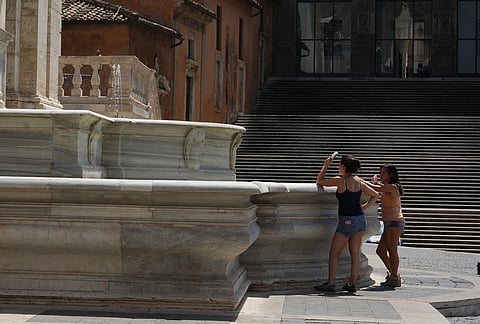 Tourists use handheld fans as they pause in Piazza del Campidoglio on Rome's Capitoline Hill, Saturday, Aug. 1, 2026. 
