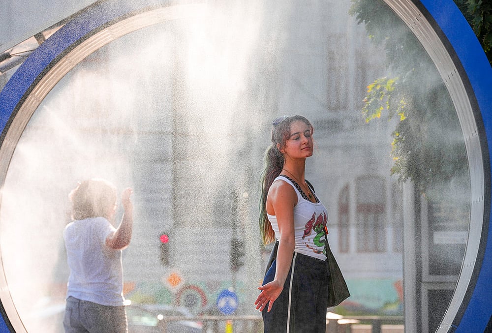 A woman pauses while she walks through a water mist machine installed by city administration to assist people in coping with the heat, as the National Weather forecaster issued an extreme heat code red warning for most parts of the country, in Bucharest, Romania, Thursday, Aug. 6, 2026.  - | Photo: AP/Vadim Ghirda