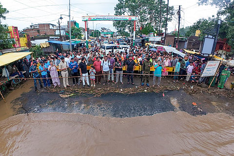 Local residents and commuters gather behind police barricades after security personnel and SDRF teams stopped traffic movement along a bridge submerged under swelling Narmada floodwaters following continuous heavy rainfall, in Dindori district, Madhya Pradesh.