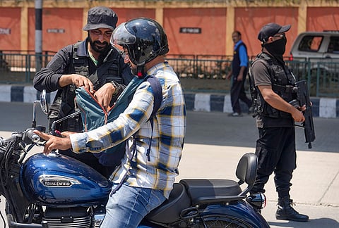 A security official from the Special Operations Group (SOG) of Jammu and Kashmir Police searches the backpack of a motorcyclist as part of intensified security checks and frisking drives ahead of Independence Day, near Bakhshi Stadium, in Srinagar.