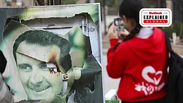 A woman uses her mobile phone near a damaged picture of ousted Syrian ruler Bashar al-Assad as people celebrate, after the Syrian opposition announced that they have ousted President Bashar al-Assad, in Qamishli, Syria December 8, 2024. - | REUTERS/Orhan Qereman