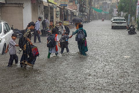 Women along with children move on a waterlogged road amid rainfall, in Patiala, Punjab, Friday, Aug. 14, 2026. 