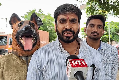 Khandwa Municipal Corporation Leader of Opposition Deepak Mullu Rathore speaks to the media while a supporter dressed in a dog costume stands behind him during a protest alleging corruption in the municipality's stray dog sterilization programme, in Khandwa, Madhya Pradesh.