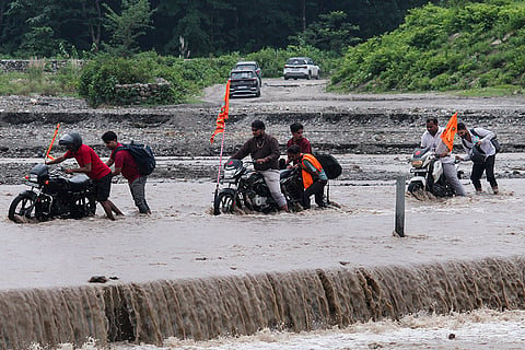 People push two-wheelers through the swollen Bin river after incessant rainfall, in Rishikesh.