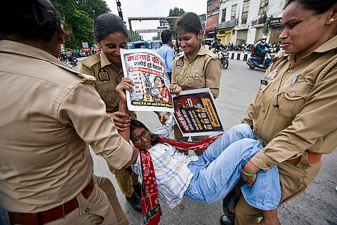 Police personnel detain a Samajwadi Party supporter during a protest against inflation on food items, at Hazratganj crossing, in Lucknow.
