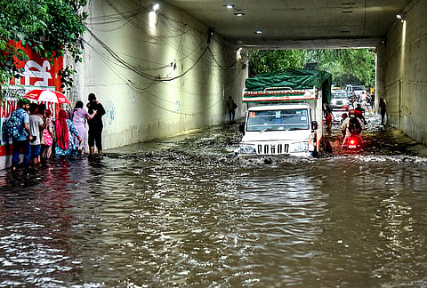 Commuters wade through the waterlogged Zakhira railway underpass following rainfall, in New Delhi. 