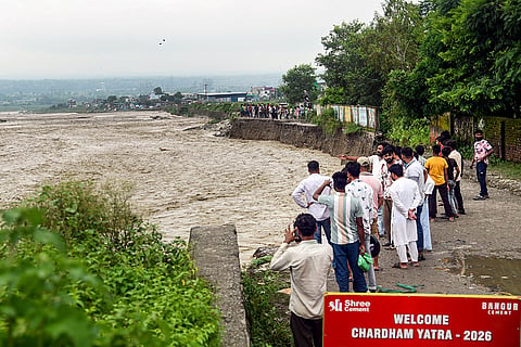 People look at the swollen Swarna river flowing in spate after monsoon rains, in Dehradun.