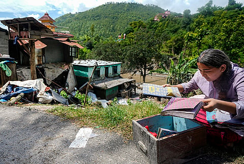 A student looks at books in a box retrieved from debris in the aftermath of the recent flash floods, in Galchhi, Dhading district, Nepal, Sunday, Aug. 30, 2026. 