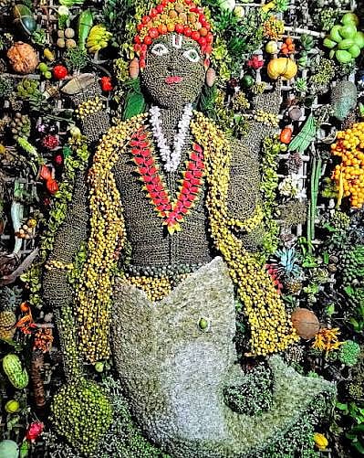 Decorated Ganesha idol surrounded by fruits, leaves and flowers.